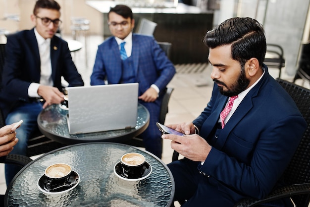 Group of indian business man in suits sitting at office on cafe with laptop texting on phones and making photo of coffee