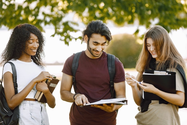 Group of international students standing together in park at university. African and caucasian girls and indian boy talking outdoors