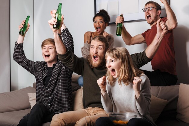 ソファに座って、家でチップスとビールと一緒にテレビを見ながら幸せに叫んでいる楽しい友達のグループ