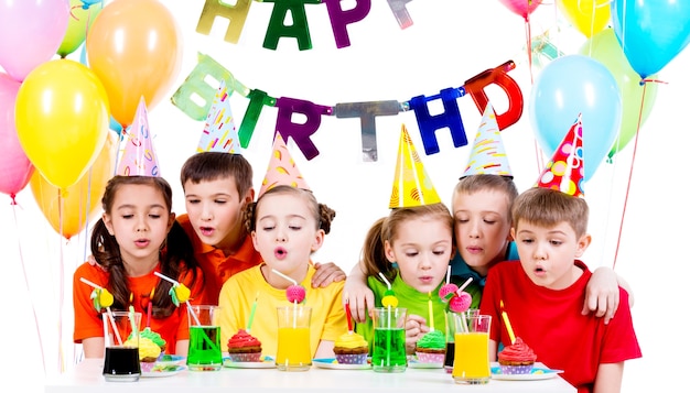 誕生日パーティーでろうそくを吹くカラフルなシャツを着た子供たちのグループ-白で隔離。