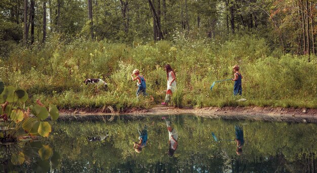 緑に覆われ、日光の下で湖に反射してフィールドを歩く子供たちのグループ