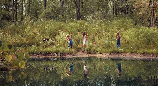 緑に覆われ、日光の下で湖に反射してフィールドを歩く子供たちのグループ
