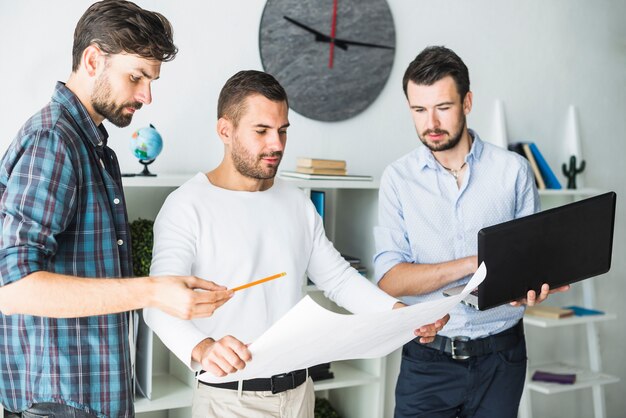 Group of male architect using laptop while looking at blueprint