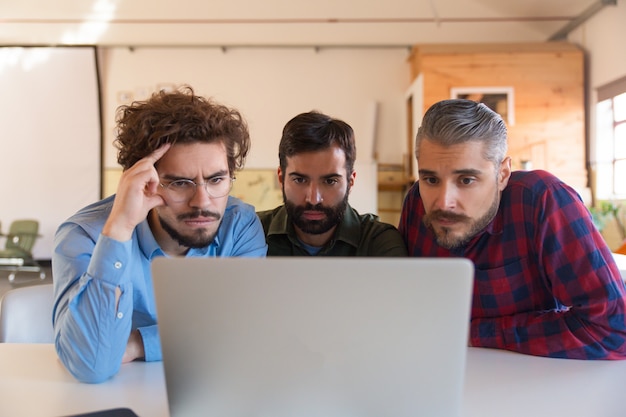 Group of male entrepreneurs in casual staring at laptop monitor