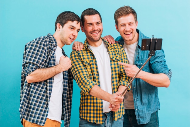 Free photo group of male friends taking selfie on mobile phone against blue backdrop