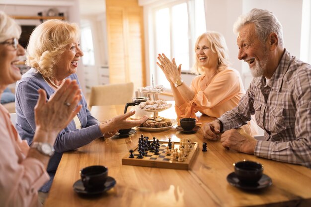 Group of mature people having fun while talking during chess game at home
