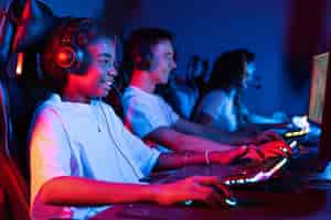 Free photo group of multiracial teens in headsets playing video games in video game club with blue and red illumination keyboard and mouse with illumination
