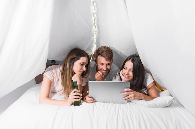 Бесплатное фото Группа друзей, лежащих на кровати, глядя на цифровой планшет
