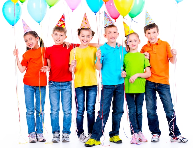 Бесплатное фото Группа счастливых детей в цветных футболках с воздушными шарами на белой стене.