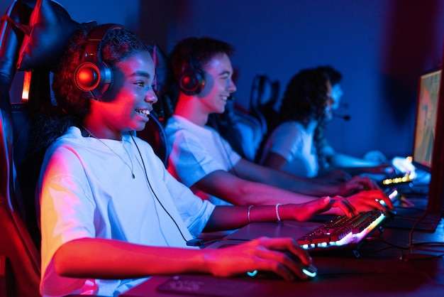 Бесплатное фото Группа многорасовых подростков в наушниках играет в видеоигры в видеоигровом клубе с синим и красным освещением клавиатура и мышь с освещением