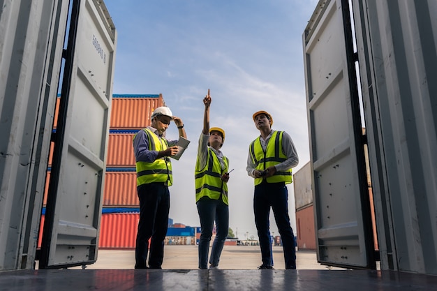 Группа штатных работников, стоящих и проверяющих коробку контейнеров с грузового судна для экспорта и импорта Premium Фотографии
