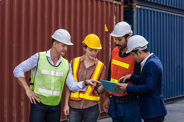 Группа штатных работников, стоящих и проверяющих коробку контейнеров с грузового судна для экспорта и импорта