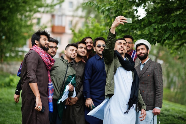 Gruppo di uomini pakistani che indossano abiti tradizionali salwar kameez o kurta che fanno selfie sul telefono cellulare