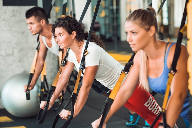 Group of people doing workout with fitness strap in health club