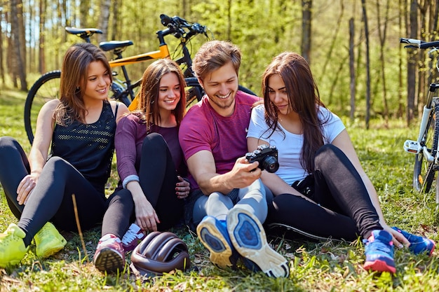 Foto gratuita un gruppo di persone che guardano foto su fotocamere compatte e si rilassano dopo un giro in bicicletta in una foresta.