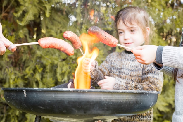 Group of people roasting sausages on burning barbecue at outdoors