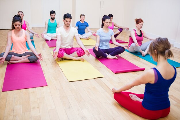 Group of people and trainer sitting in lotus position