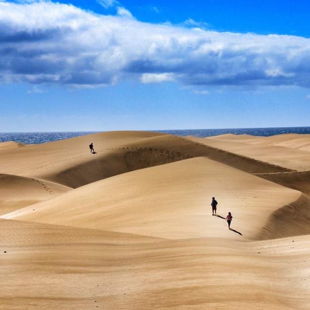 Group of people walking over sand dunes under a cloudy sky