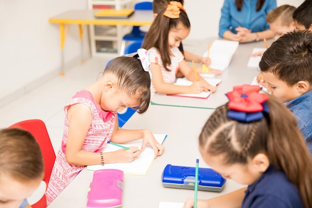 教室でライティングの割り当てに取り組んでいる就学前の子供たちのグループ