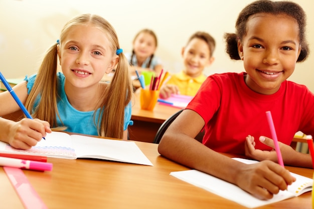 Group of schoolchildren with pencils and notebooks in classroom