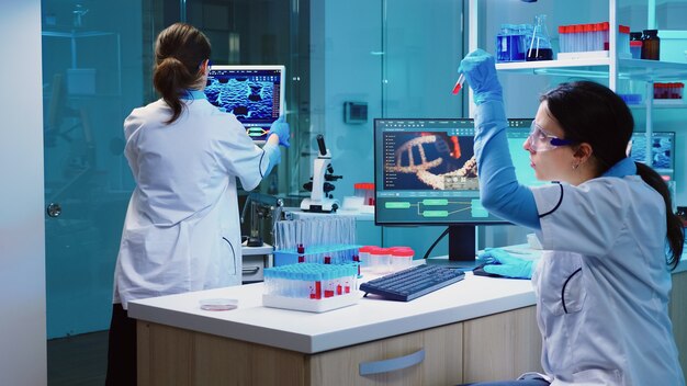 試験管や科学機器で生化学サンプルを調べながら、実験室で働く白衣を着た科学者のグループ