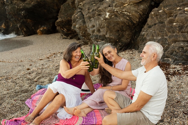 Foto gratuita gruppo di amici anziani che esultano con la birra in spiaggia