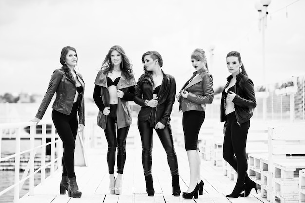 Group of sexy models girls in black bra and leather jackets on the dock