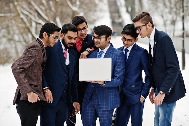 スーツを着た6人のインド人ビジネスマンのグループがラップトップを探してヨーロッパで冬の日に屋外でポーズをとった