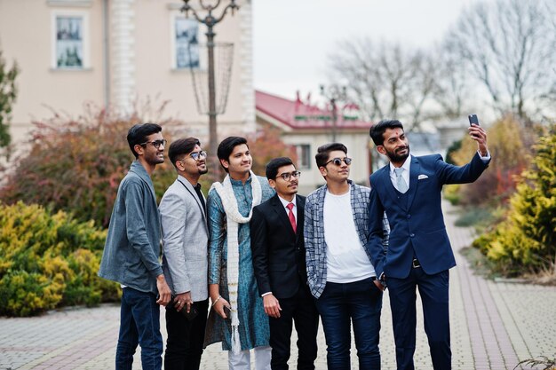 Group of six south asian indian mans in traditional casual and business wear standing and making selfie at mobile phone together