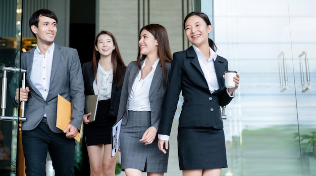 Group of smart young asian businessmale and female formal dress walking pass modern office entrance with confident and happiness