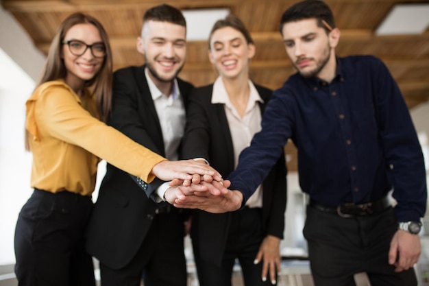 Gruppo di soci d'affari sorridenti in giacca e cravatta che mostrano unità con le mani insieme mentre trascorrono del tempo in un ufficio moderno