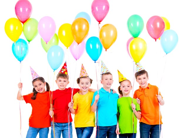 Group of smiling children in colored t-shirts and party hats with balloons on a white background