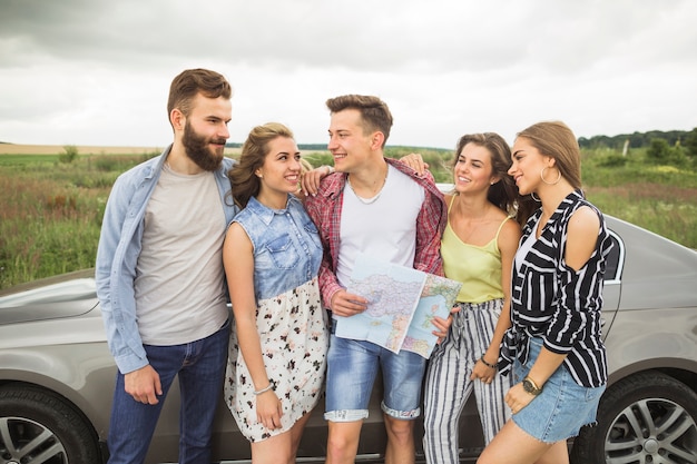 Group of smiling friends standing by the car looking at each other