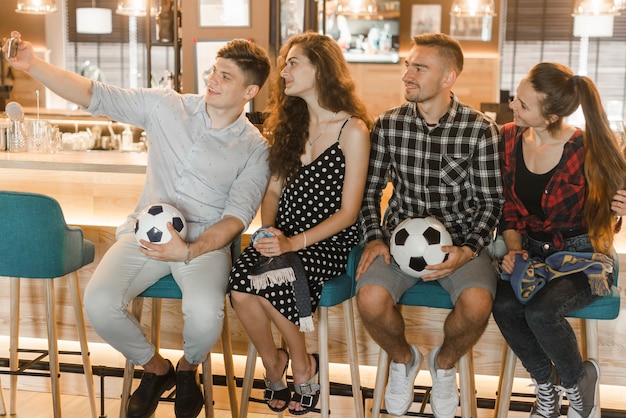 Gruppo di tifosi di calcio seduti in bar prendendo selfie su smart phone