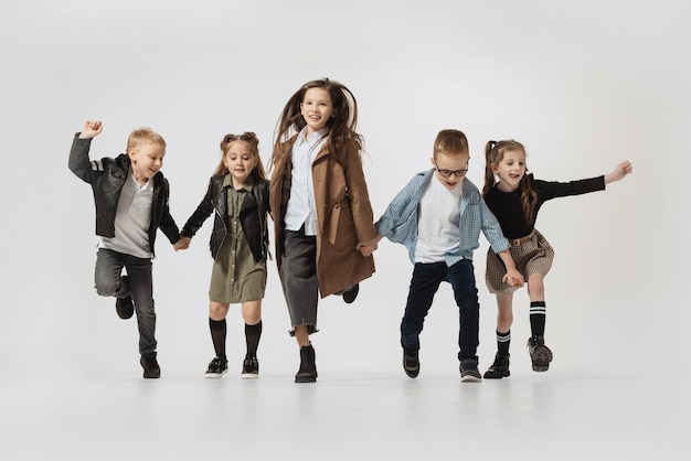 Group of stylish children running jumping posing isolated over grey studio background Retro fashion style