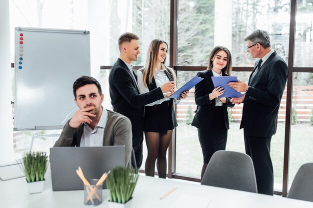 Group of successful  businesspeople using a folder  together in front of office building windows overlooking the city.