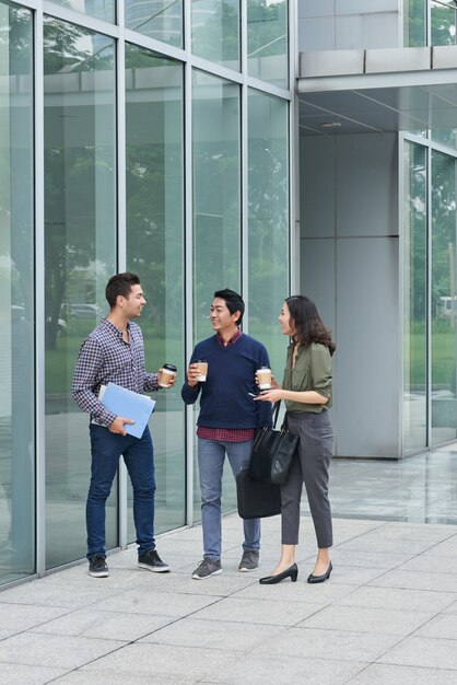 A group of three colleagues waalking outdoors with takeaway coffee at a lunch break