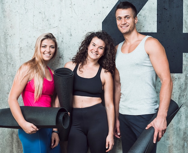 Group of three happy young people with fitness mat