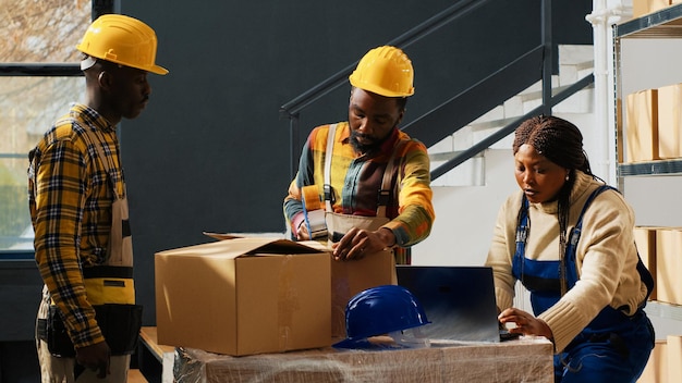 Group of trained workers using depot equipment, working in packaging department with packages. People using merchandise boxes to pack and ship products, industrial stock distribution.