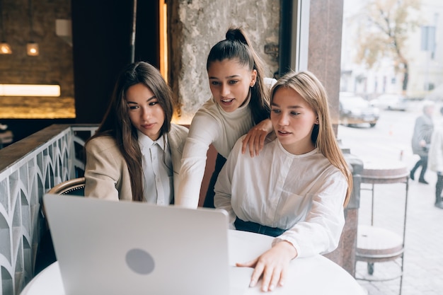 A group of women friends in a cafe are looking at a laptop