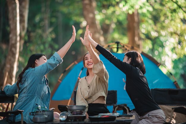 Group of women giving five to each other on camping with toothy smile and happy together at front of camping tent in forest