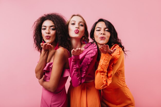 Группа женщин, отправляющих воздушные поцелуи на розовую стену