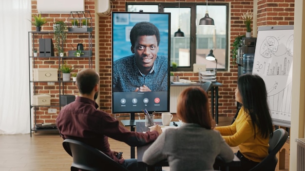 Группа работников использует удаленный видеозвонок, чтобы поговорить с мужчиной о росте бизнеса на компьютере. Группа людей встречается, чтобы обсудить маркетинговое сотрудничество на онлайн-телеконференции в Интернете.
