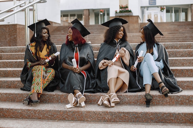 Gruppo di giovani studentesse afroamericane vestite con un abito nero di graduazione. campus come sfondo