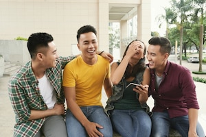 Group of young asian men and girl sitting together in urban street and laughing