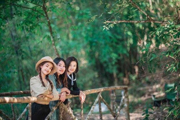 竹の橋の上に立っている若いアジアの女性のグループは、一緒に幸せで森でキャンプしながら美しい自然を探しています