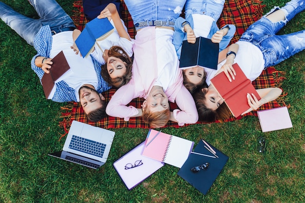 A group of young beautiful people lie on the grass. Students relax after classes at the campus