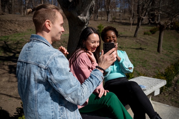 Group of young friends celebrating the lifting of face mask restrictions outdoors and using smartphones