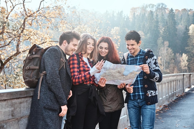 若い人たちのグループが秋の森を歩いている間、彼らがいる地図を見ています。