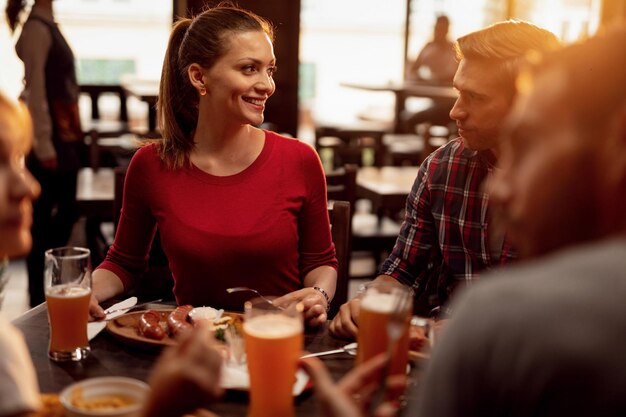 Group of young people having lunch and talking to each other in a pub Focus is on happy woman